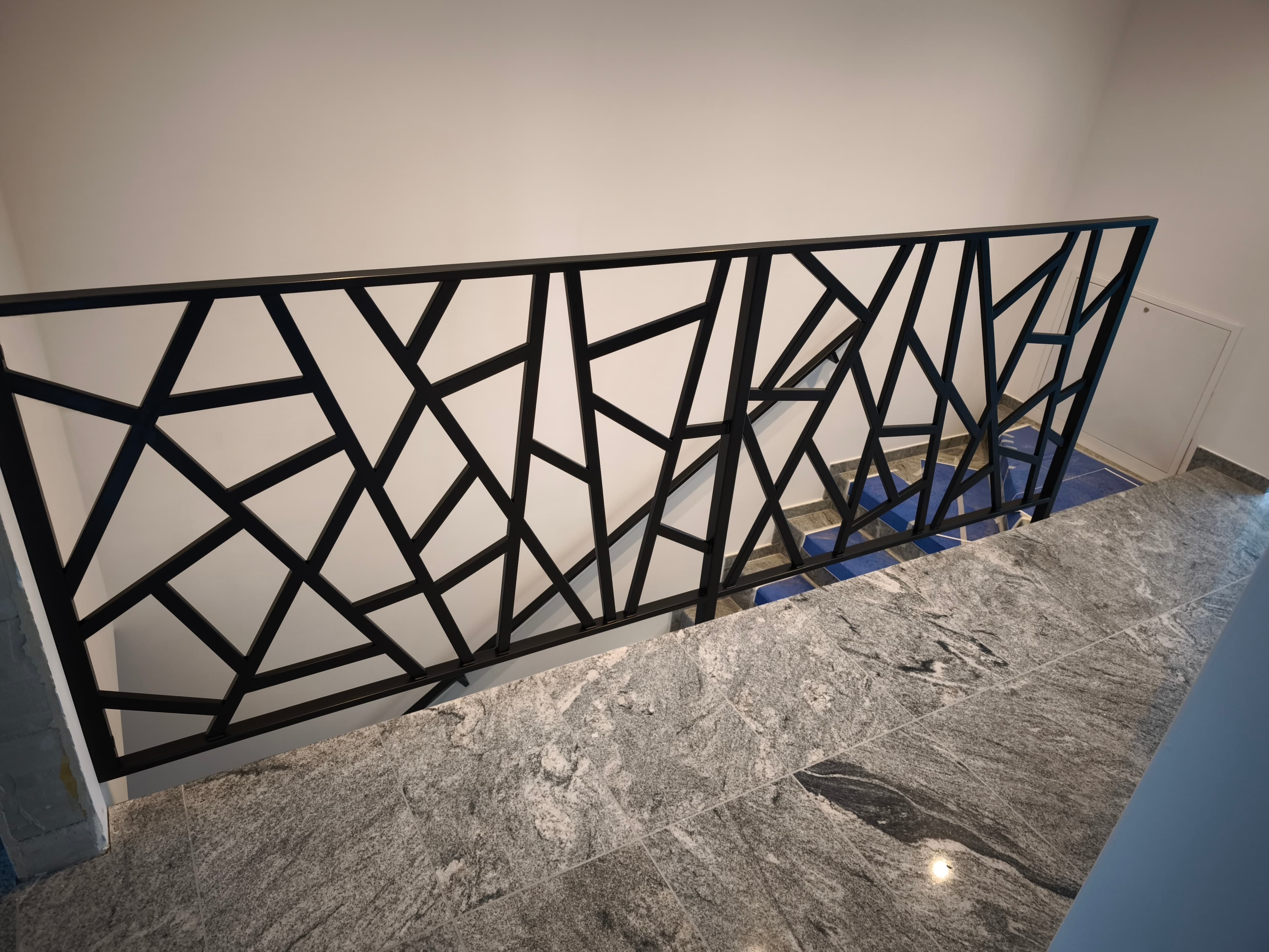 Czarna balustrada geometryczna na schodach z niebieskim wykończeniem